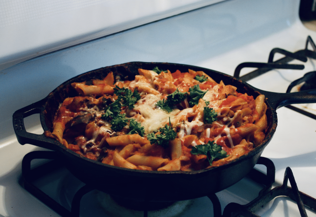 sausage pasta bake on stove in a black skillet with cheese on top