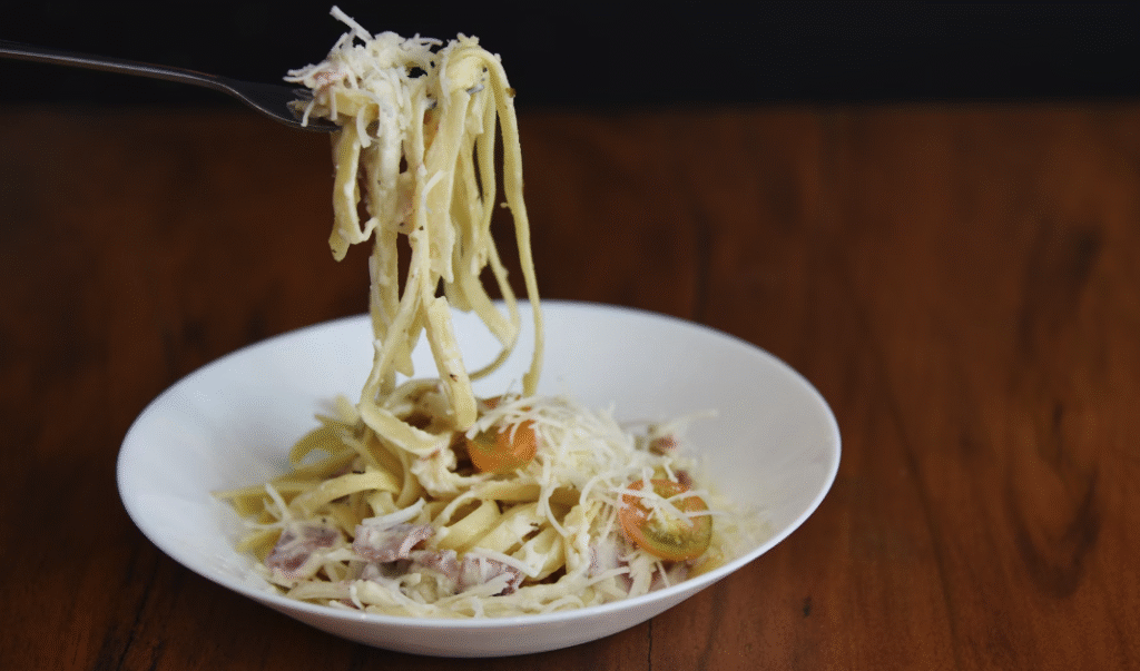 ham pasta in a white bowl being lifted with a fork