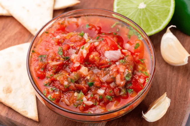 bowl of tomato salsa surrounded by lime, garlic and tortillas